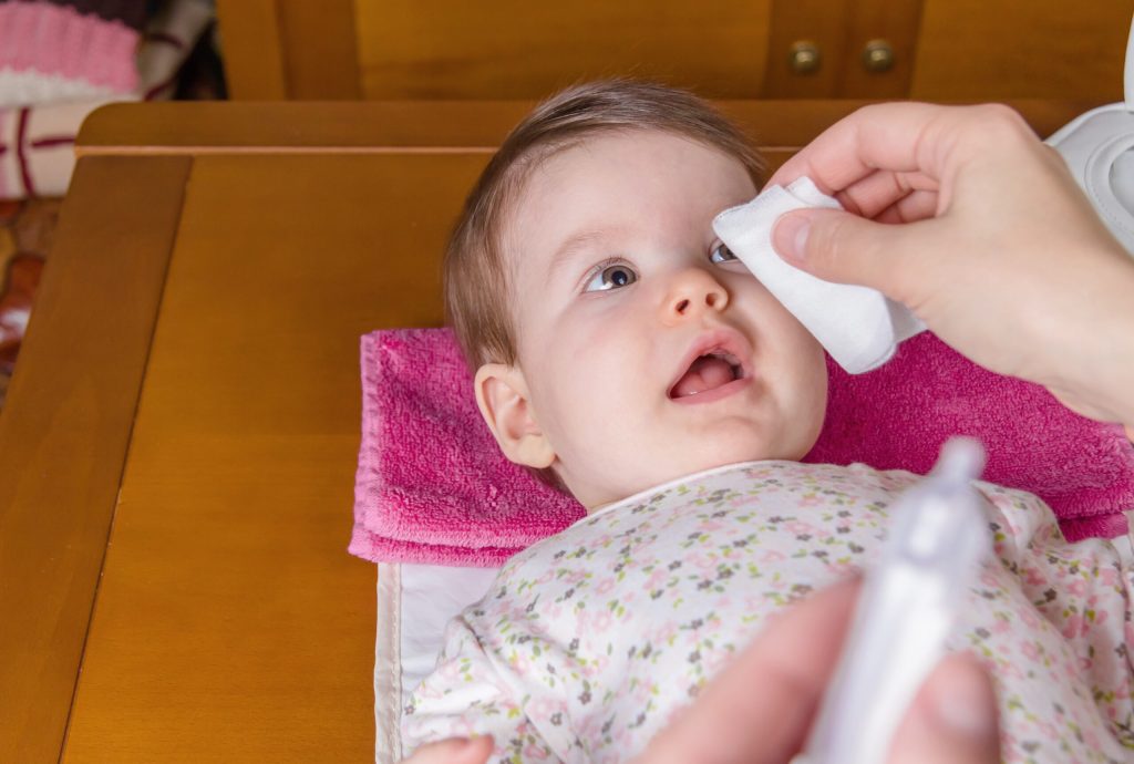 closeup of mother hands cleaning eyes of baby with physiological serum in cotton scaled 1