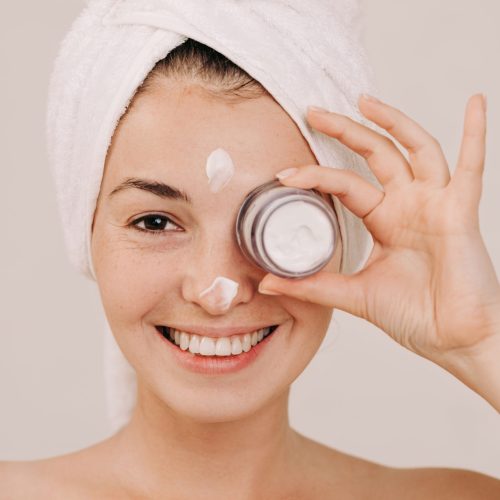 Portrait of beautiful woman in towel holding jar of face cream