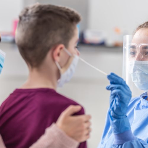 Mom holds her son as medical worker takes sample from his nose during coronavirus pandemic testing.